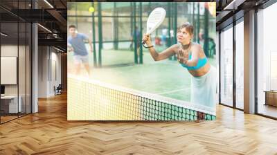 Caucasian woman in tank top and skirt playing padel tennis match during training on court. Wall mural