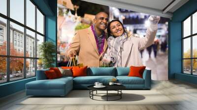 Cheerful married couple looking for decorations on Christmas street market while shopping Wall mural