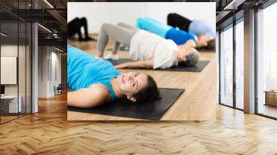 Class of male and women of different ages in active wear doing buttock bridge exercise during Pilates training together in gym Wall mural