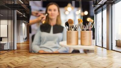 Closeup of set of cosmetic brushes in two organizers on table in beauty salon with makeup artist working with female client on blurred background Wall mural