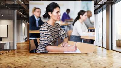 Concentrated asian woman listening to lecture in classroom with group of adult people. Postgraduate education concept.. Wall mural