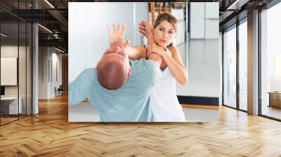 Concentrated girl practicing effective self defence techniques with coach in training room, using palm to launch blow in chin.. Wall mural