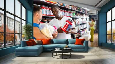 Confident African seller offering diet and sports supplements to interested athletic person in sports nutrition store Wall mural