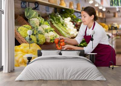 Delighted young saleswoman placing fresh tomatoes on food stall in grocery store Wall mural