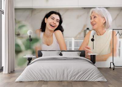 Elderly mother and adult daughter drinking tea and chatting happily at home Wall mural