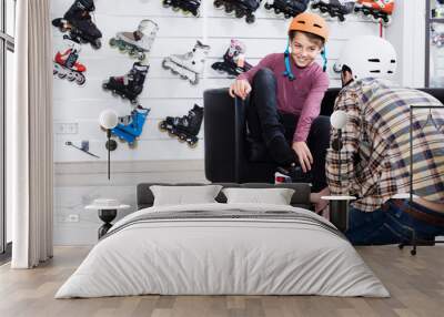 father assisting son in trying on roller-skates in sports store Wall mural