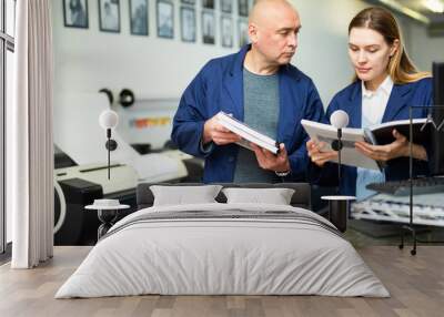 Female publishing facility worker reading operation manual for large printer. Her male co-worker standing beside. Wall mural