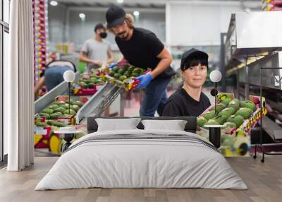 Fine woman working at fruit warehouse carrying box with sorted avocados. Wall mural