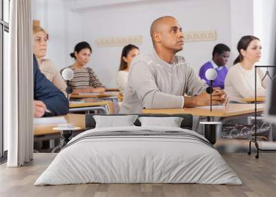 Focused adult latin american man listening to lecture in classroom with group. Postgraduate education concept Wall mural