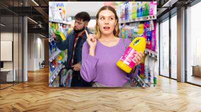 Focused people making purchases in household chemistry store, woman choosing detergent, man on background Wall mural