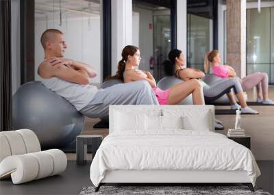 Focused young adult man doing workout with fitness ball during group pilates training Wall mural