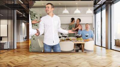 Genial young man in casual attire extending warm handshake to friend, welcoming to enjoyable home dinner event Wall mural