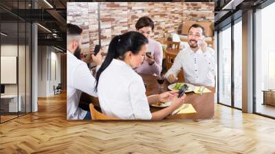 Group of friends using smartphones at restaurant table and chatting. Wall mural