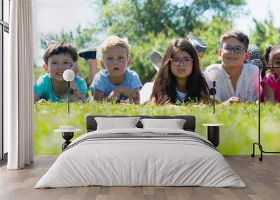 Group of happy children resting on grass and smiling together in park Wall mural