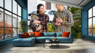 Happy adult couple, man and woman, standing with kitten outdoor near their house Wall mural