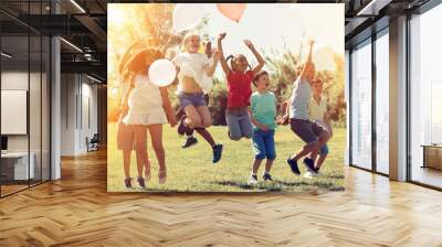 Happy children holding ballons and  jumping  together in park Wall mural