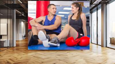 happy greek female boxer is sitting with man and talking about healthy in gym. Wall mural