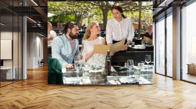 Hospitable waitress helping visitors with menu on outdoor terrace of country restaurant Wall mural