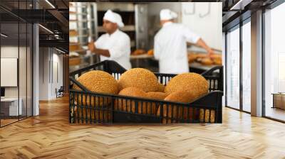 Hot bread in crate on table in small bakery, bakers working on background Wall mural