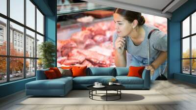 In local butcher shop, customer girl looks thoughtfully at glass display case of refrigerator and chooses pork wing ribs Wall mural