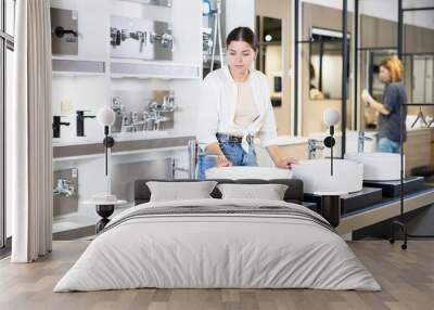 in plumbing department,thoughtful woman inspects round white ceramic sinks with faucets.buyer inspects goods in window Wall mural