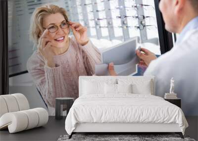 male optician offering glasses frames to elderly woman Wall mural