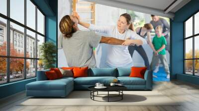 Man and woman at group self-defense lesson are learning new technique of blowing to chin, trainer is practicing technique with children in background Wall mural