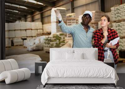 Man having conversation with young woman about documentation in warehouse, pointing to something Wall mural