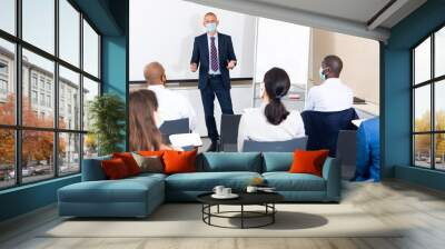 Man in protective mask giving presentation to colleagues at international business meeting Wall mural