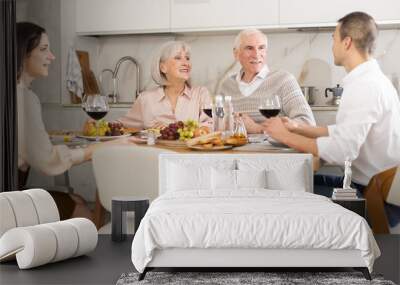 Mature couple are sitting at table, chatting sweetly, discussing and telling news, sharing plans with adult children. Senior woman and man celebrate housewarming party with middle-aged guests spouses Wall mural