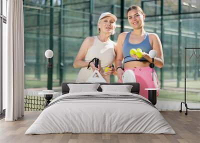 Mature smiling female padel player with her young daughter standing ready for game in court Wall mural