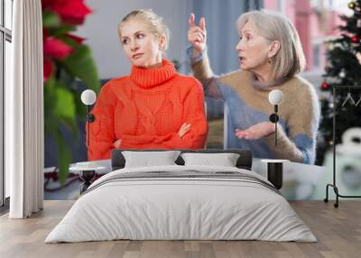 Mature woman quarrels with her adult daughter, who came to visit her before Christmas, scolding her Wall mural