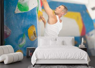 Motivated young guy practicing rock-climbing in large indoor climbing area Wall mural