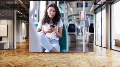 Oriental woman sitting inside tram with smartphone in hand. Wall mural