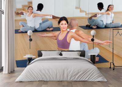 People doing stretching exercises in pairs in modern fitness center Wall mural