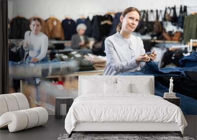 Pleased middle-aged woman choosing jean pantaloons in clothing store with large assortment Wall mural