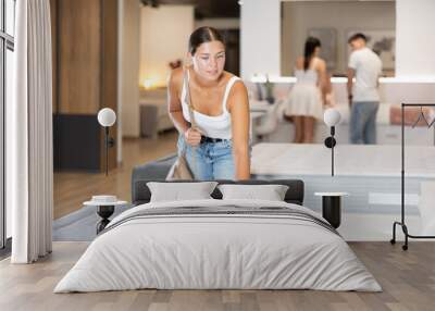 Pleased young girl choosing convenient mattress in large furniture shop Wall mural