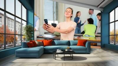 Portrait of a confident girl student taking a selfie in a university auditorium during a study break, sitting at a desk Wall mural