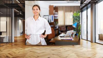 Portrait of a smiling young female employee standing in a well-lit office of a large company. Close-up portrait Wall mural