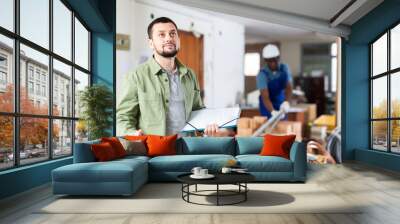 Portrait of caucasian man construction manager with paper folder standing in building site. Wall mural