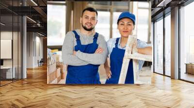 Portrait of confident positive female and male construction workers in blue workwear standing inside building under renovation.. Wall mural