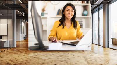 Portrait of confident smiling latin american female office employee during daily work with computer Wall mural