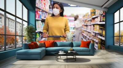 Portrait of focused Hispanic woman wearing protective mask choosing food products in grocery shop. Concept of shopping and social distancing in pandemic Wall mural