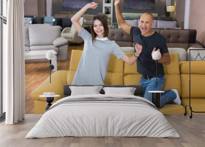 Portrait of funny happy couple jumping on yellow sofa in shopping room Wall mural