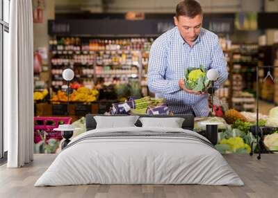 Portrait of glad cheerful positive smiling man choosing broccoli in supermarket Wall mural