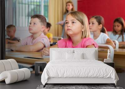 Portrait of interested blonde tween girl studying in classroom, listening to schoolteacher and writing in notebook Wall mural