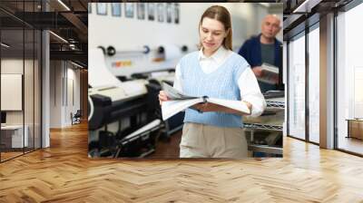 Portrait of positive female employee of a printing house with notebooks and projects in her hands Wall mural