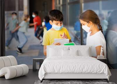 Portrait of primary school girl and boy wearing protective face masks talking outside before lesson, new normal during coronavirus pandemic situation Wall mural