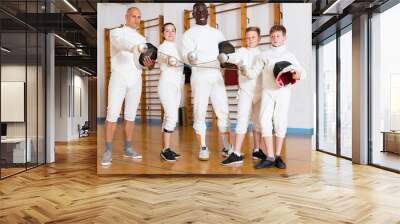 Portrait of smiling mixed age group of athletes with foils at fencing workout Wall mural