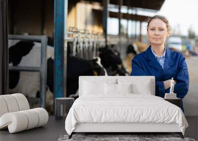 Portrait of smiling young woman working on livestock farm posing in outdoor cowshed near stall with herd of cows Wall mural